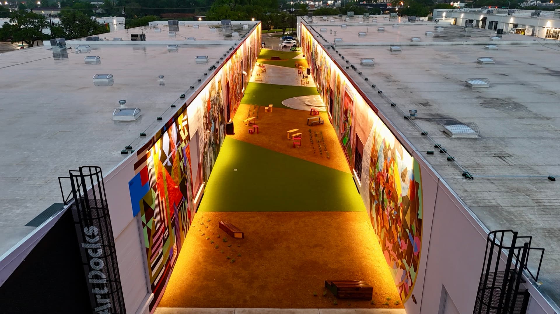 Overhead drone shot of the ArtDocks outdoor venue showing the full turf courtyard, mural walls, and entrance sign