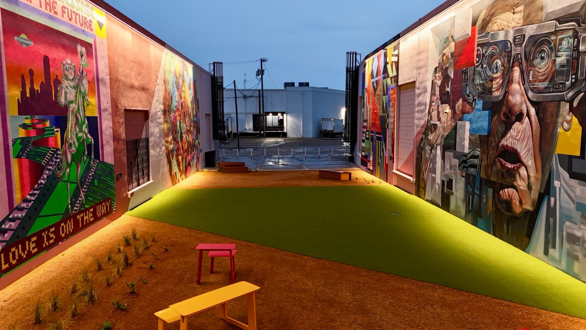 Aerial view from the entrance of the ArtDocks mural alleyway looking down the turf corridor with murals flanking both sides at dusk