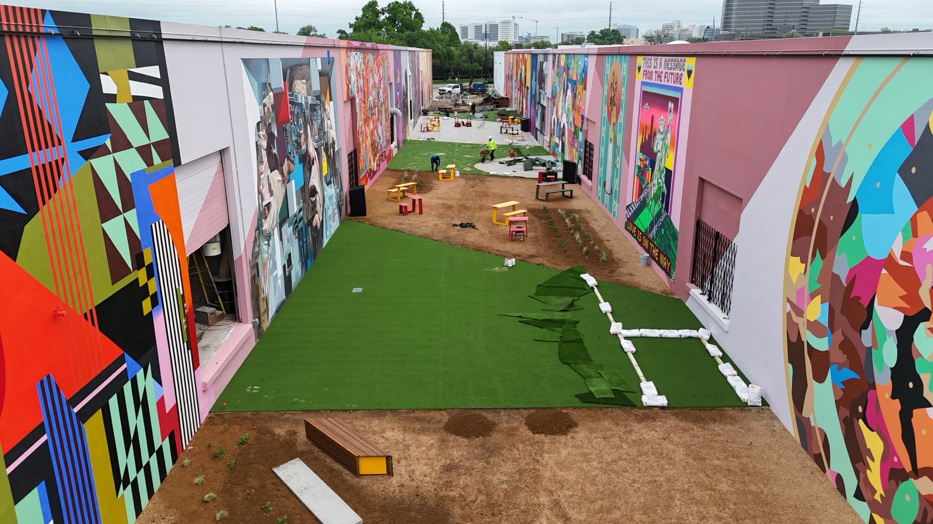 Daytime aerial progress photo of BearcatTurf artificial turf installation at ArtDocks Dallas with turf being laid and Dallas skyline visible