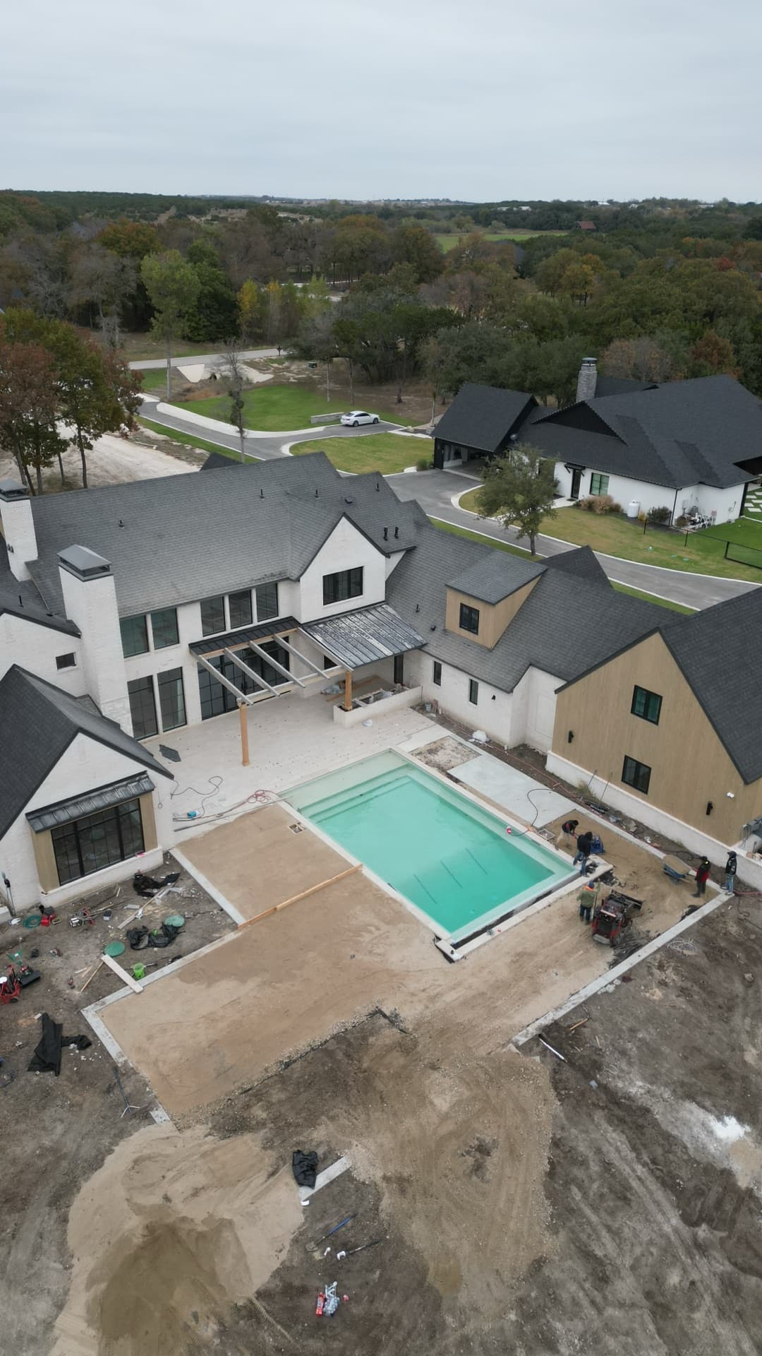 Aerial progress photo of luxury home construction with freshly filled pool, grading work, and modern white exterior under build