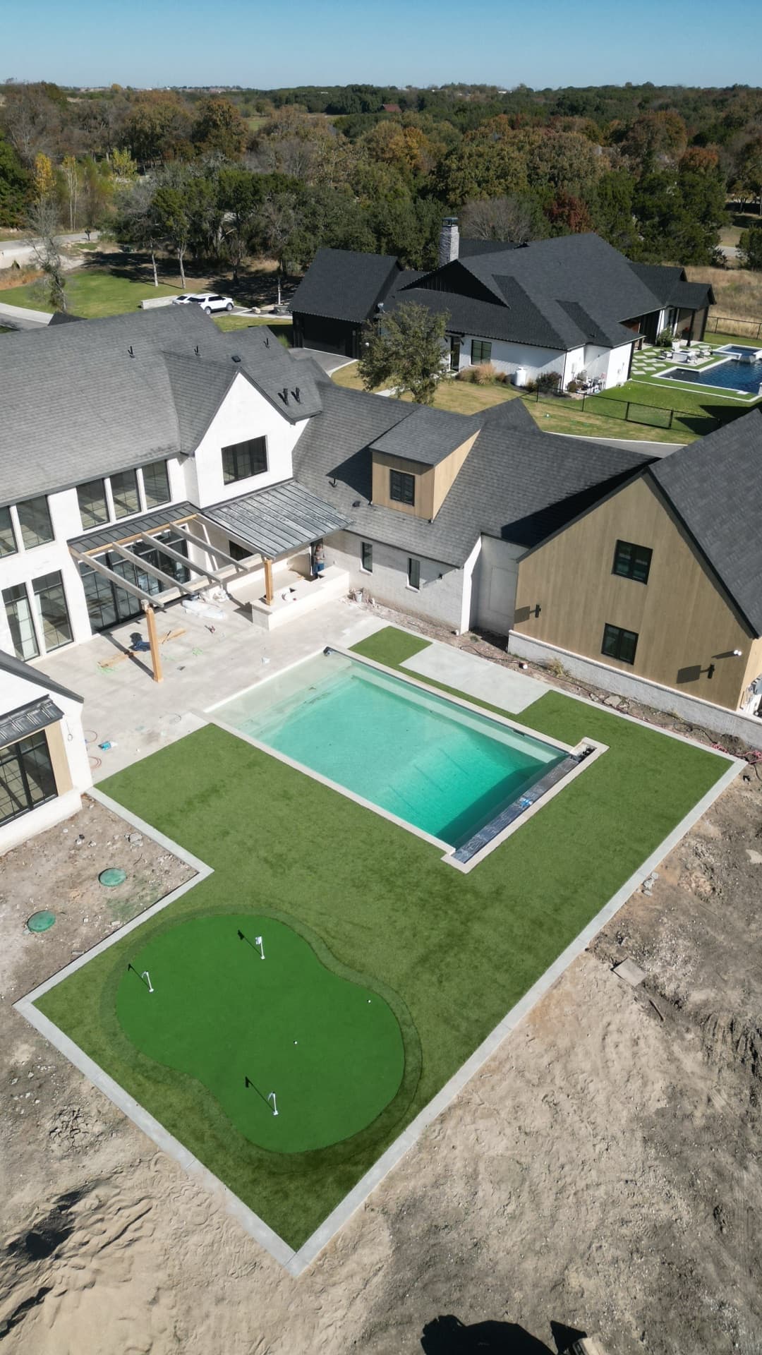 Angled aerial of luxury home backyard construction showing pool and putting green nearing completion beside modern home