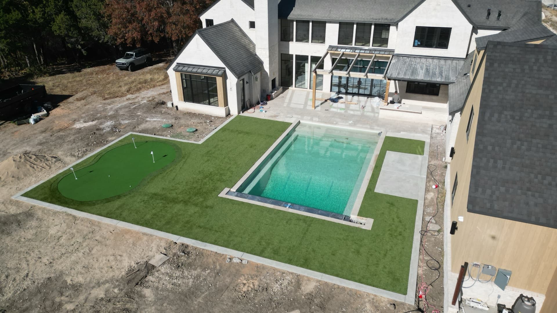 Aerial drone photo of completed luxury backyard with pool, putting green turf, and modern farmhouse under final construction