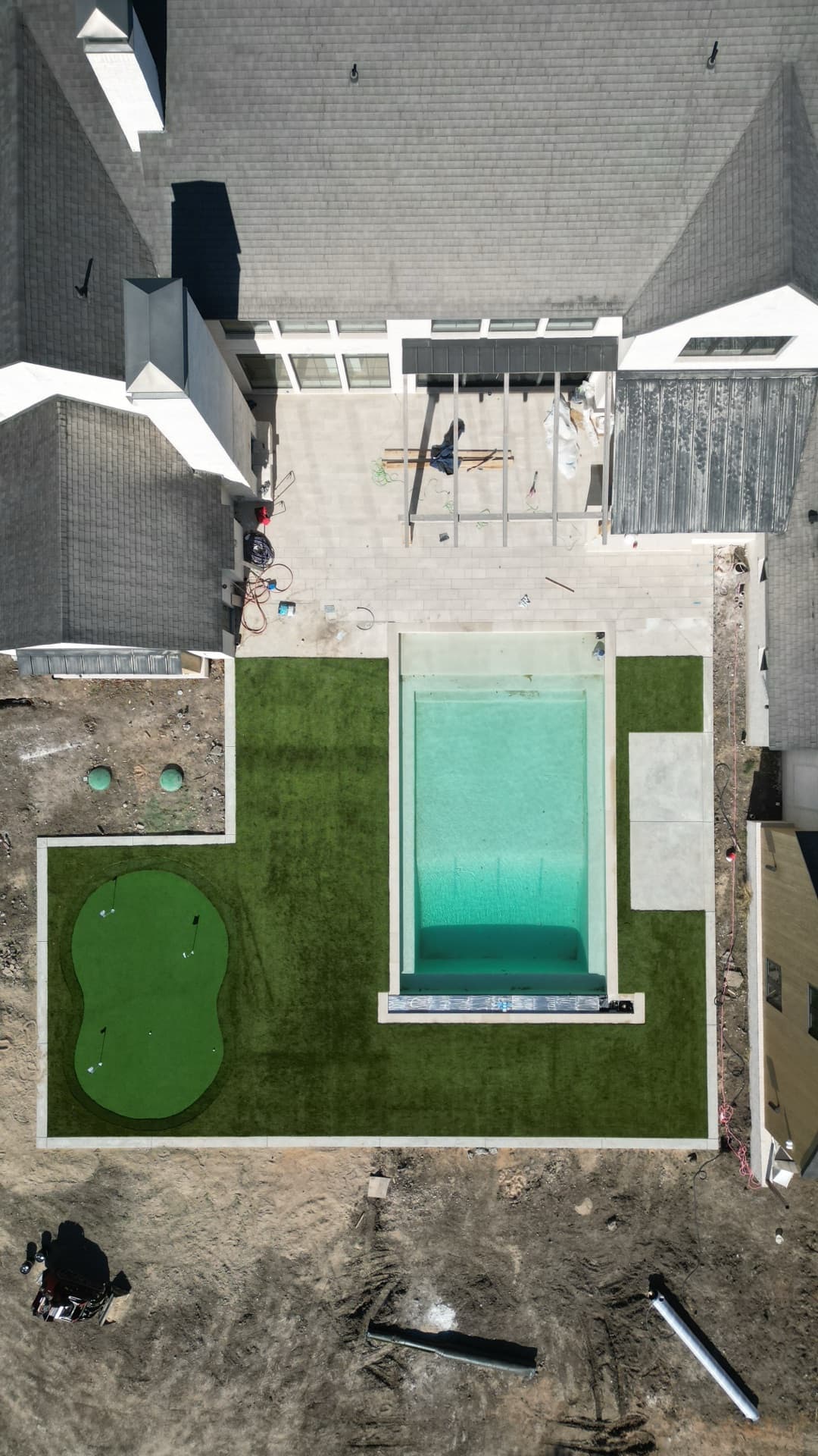 Aerial progress photo of backyard with pool and putting green turf installed, house still under construction