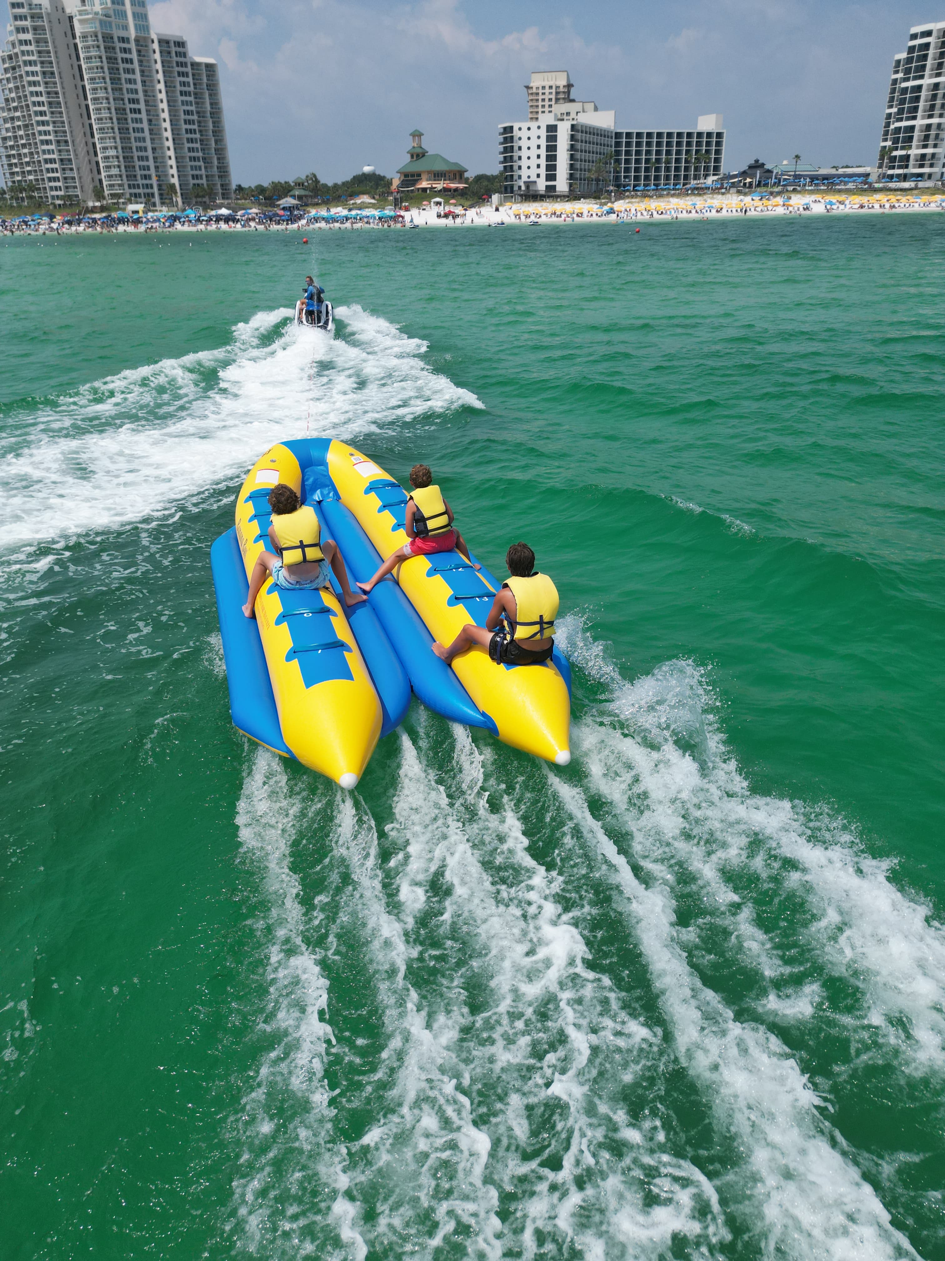 Overhead aerial drone photo of banana boats being towed on turquoise Gulf of Mexico water near Destin beach resort