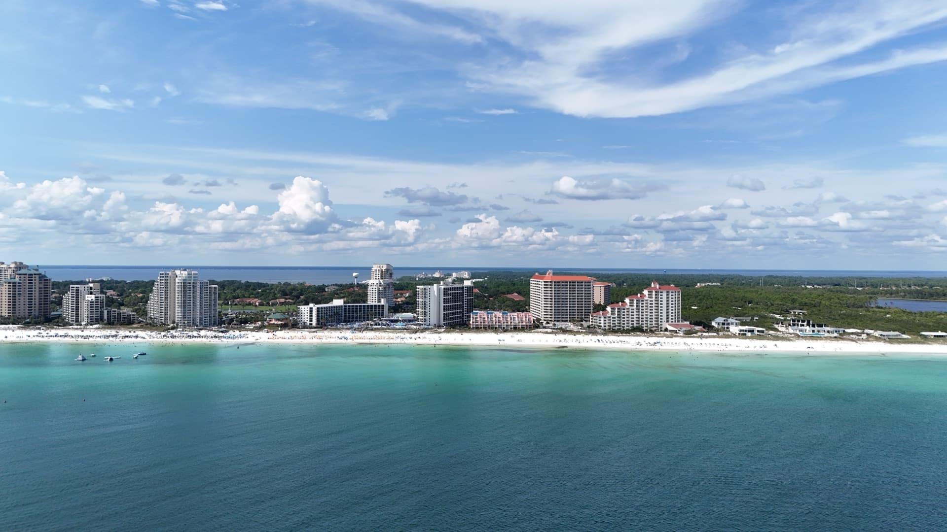 Wide aerial from Gulf of Mexico looking toward Destin Florida beach with resort hotels, white sand, and turquoise water