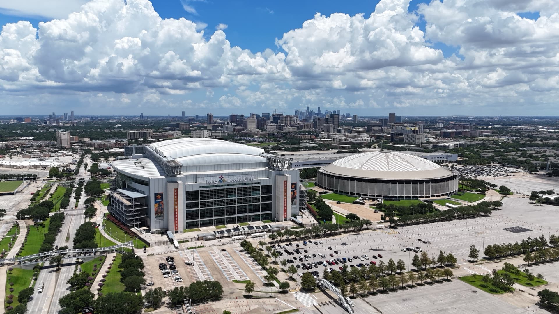 Aerial drone photo of NRG Stadium and historic Astrodome dome side by side with Houston skyline visible in the background