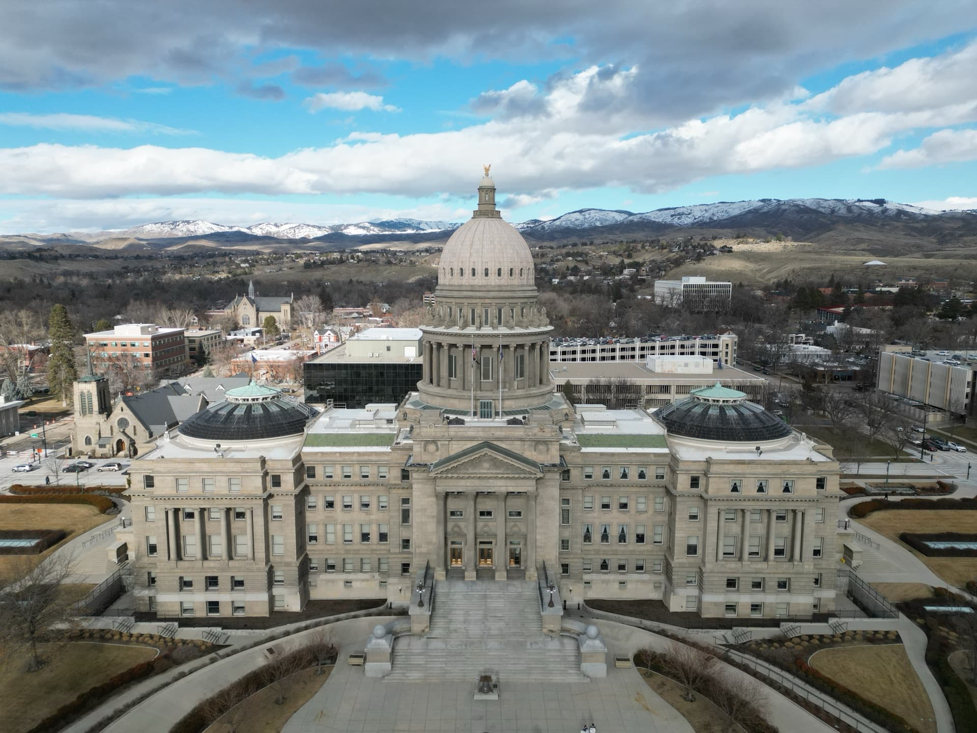 Aerial drone photo of Idaho State Capitol building in Boise with snow-capped mountains and city skyline in the background