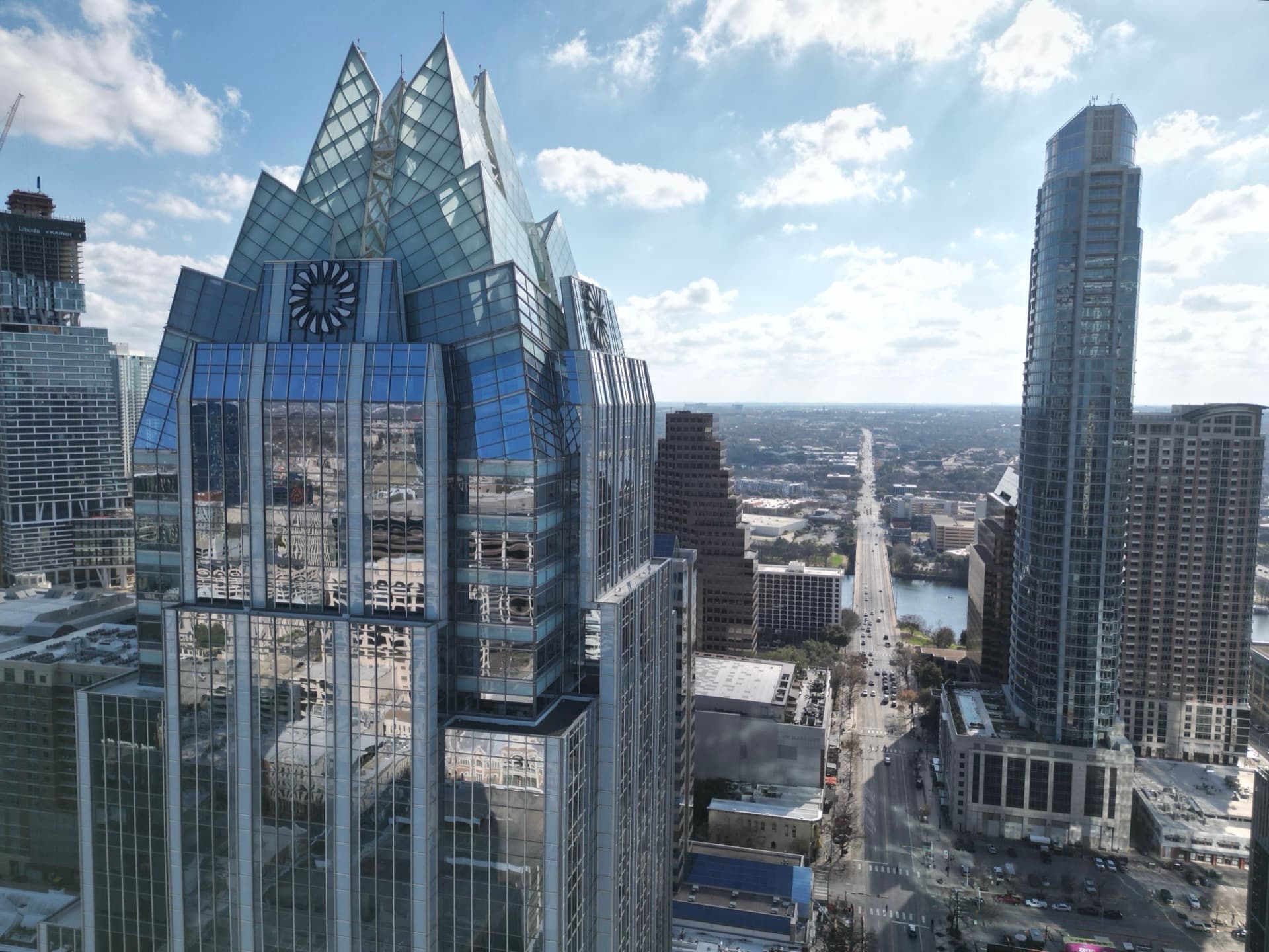 Close aerial of Austin Frost Bank Tower with its distinctive crystalline spire rising above downtown skyline and Lady Bird Lake