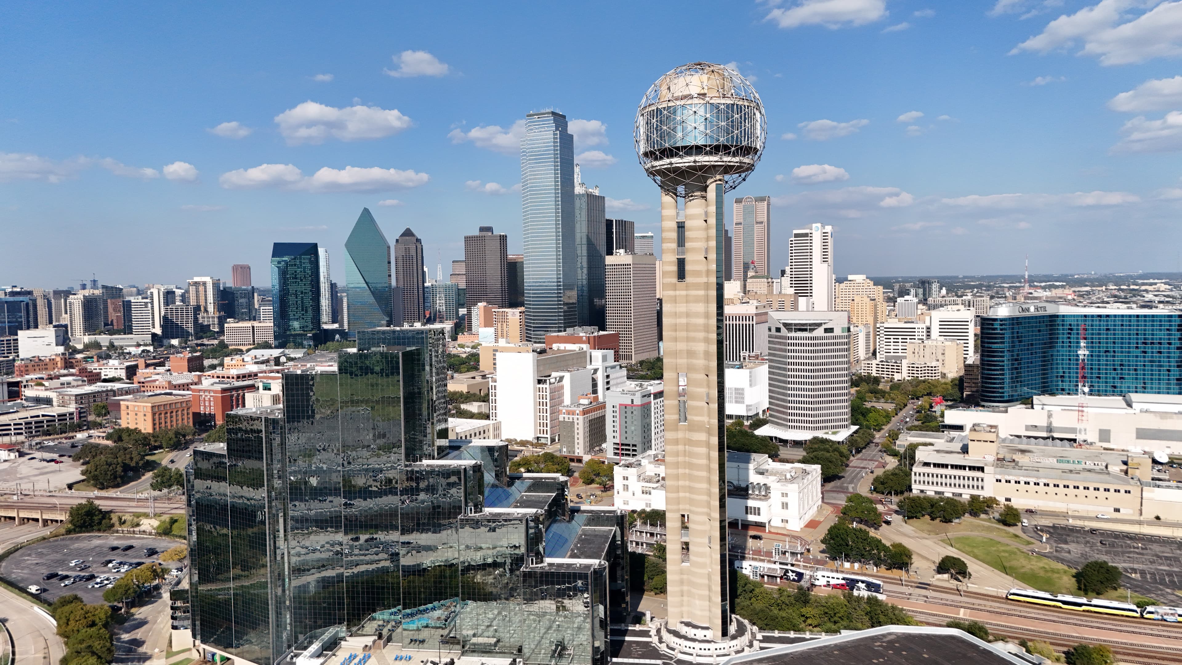 Cinematic aerial photo of Dallas Reunion Tower rising above downtown Dallas skyline with blue skies and clouds