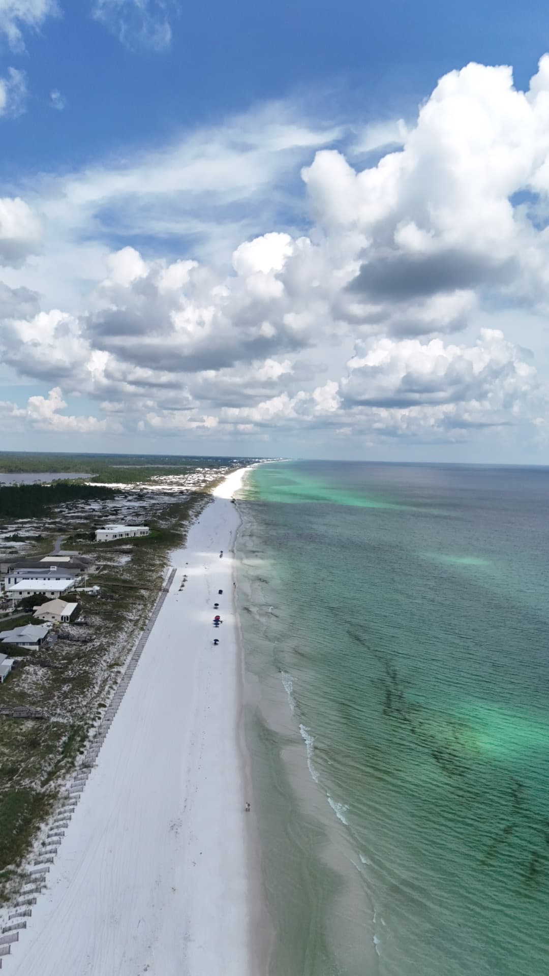 Vertical aerial of Destin beach resort strip with white sand, emerald Gulf water, and high-rise condos along coastline
