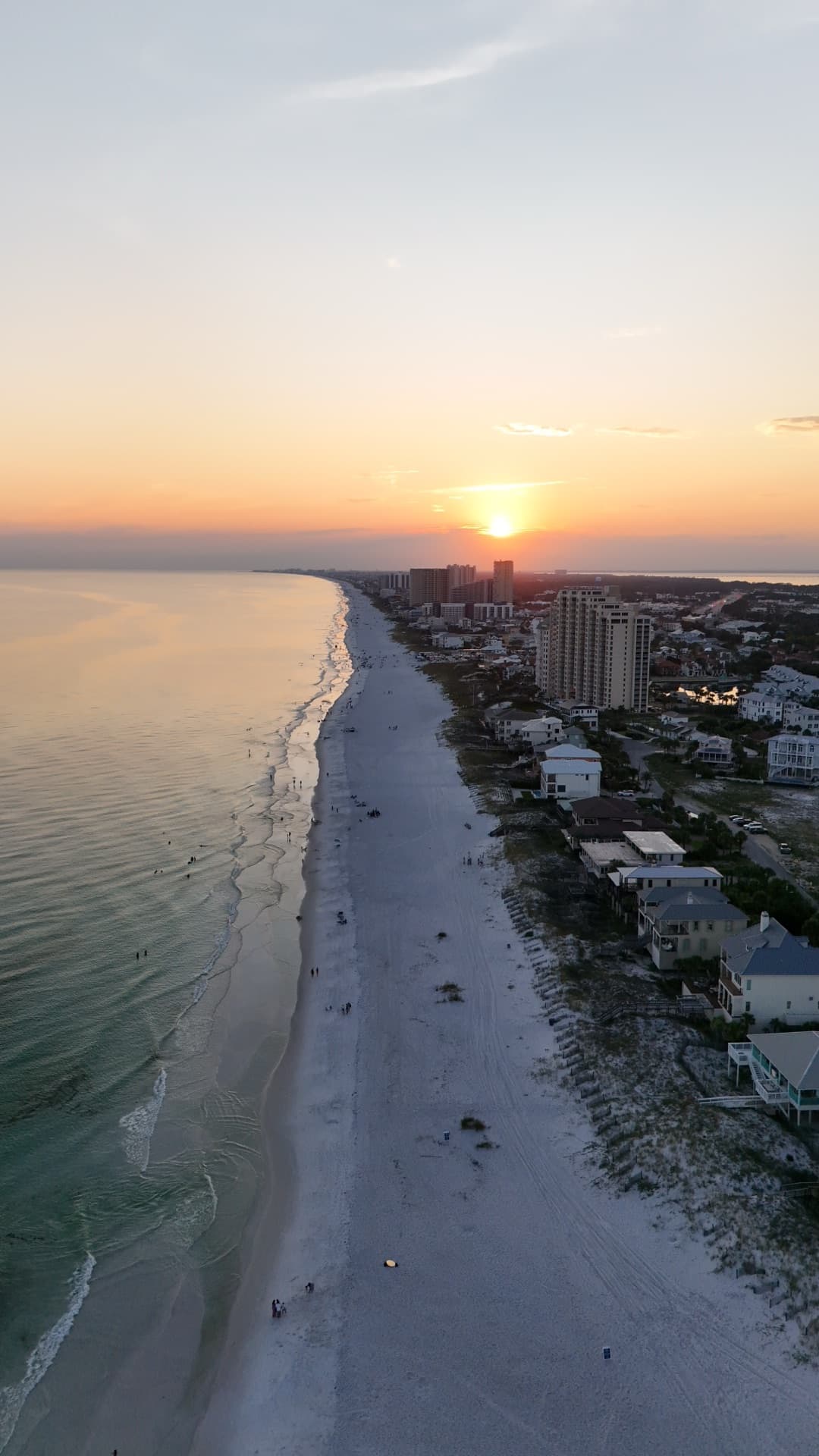 Vertical aerial of Destin Florida beach at sunset with warm golden light over resort condos and emerald Gulf water