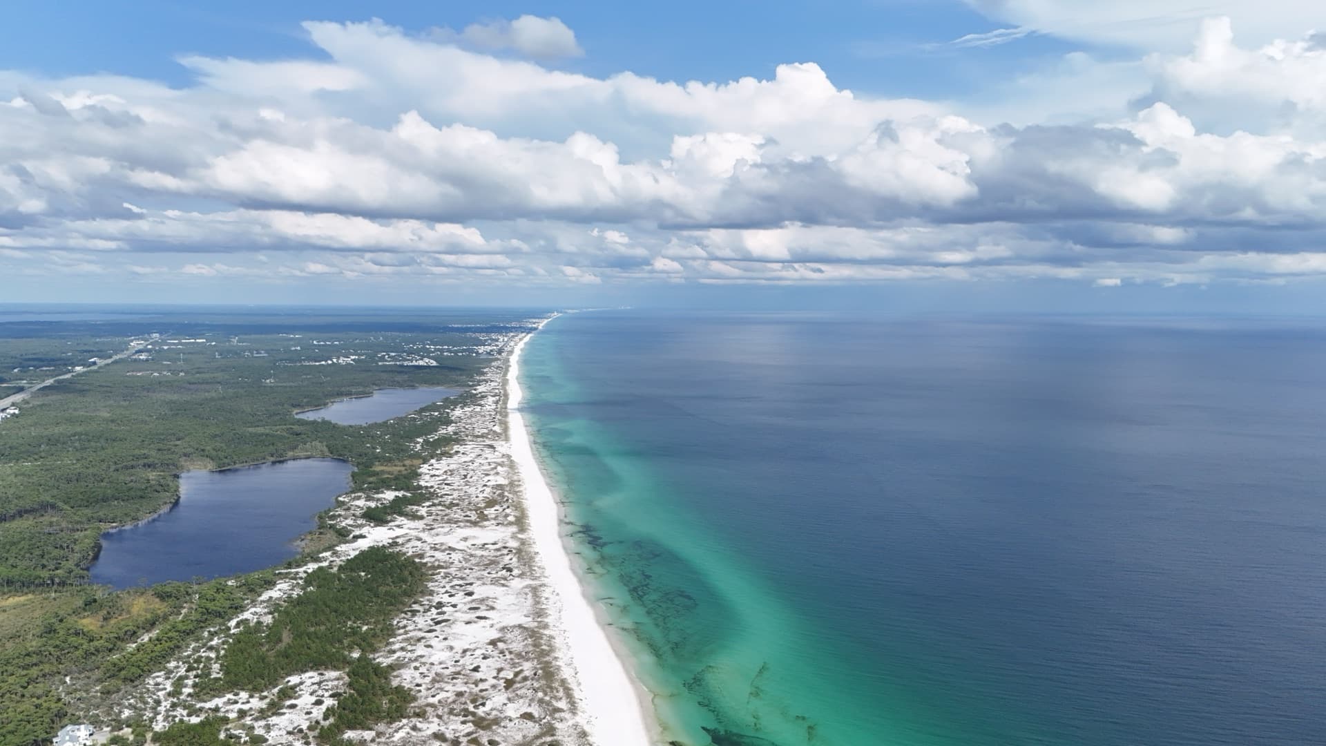 Wide aerial of Destin Florida Emerald Coast with white sand dunes, turquoise Gulf, freshwater lake, and forest stretching to horizon