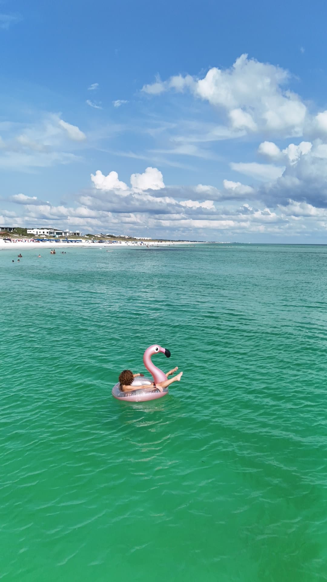 Aerial of person on pink flamingo pool float in turquoise Gulf water with Destin beach and resort skyline in background