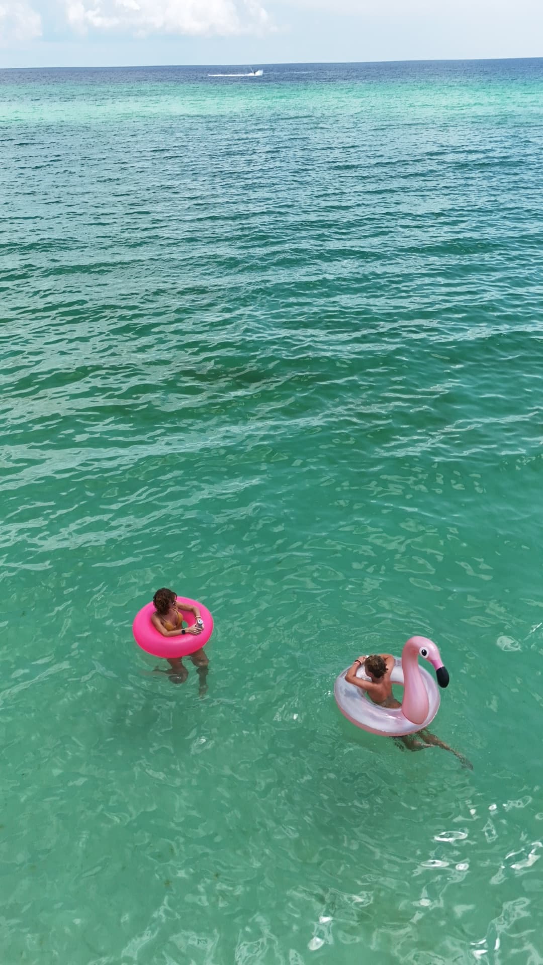 Overhead aerial of two people floating on pink flamingo pool floats in brilliant turquoise Gulf of Mexico water