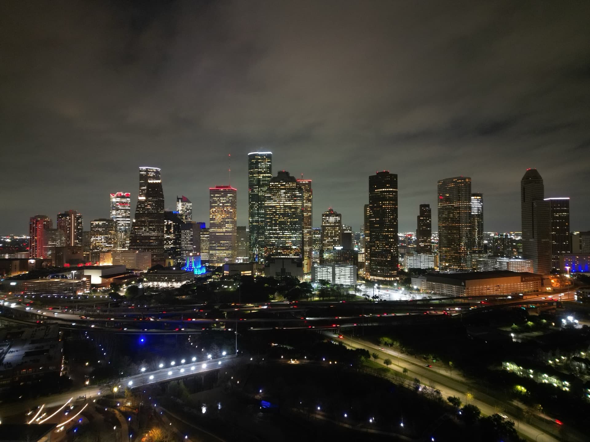 Wide night aerial of Houston city skyline with colorful building lights reflecting off bayou and freeway interchange
