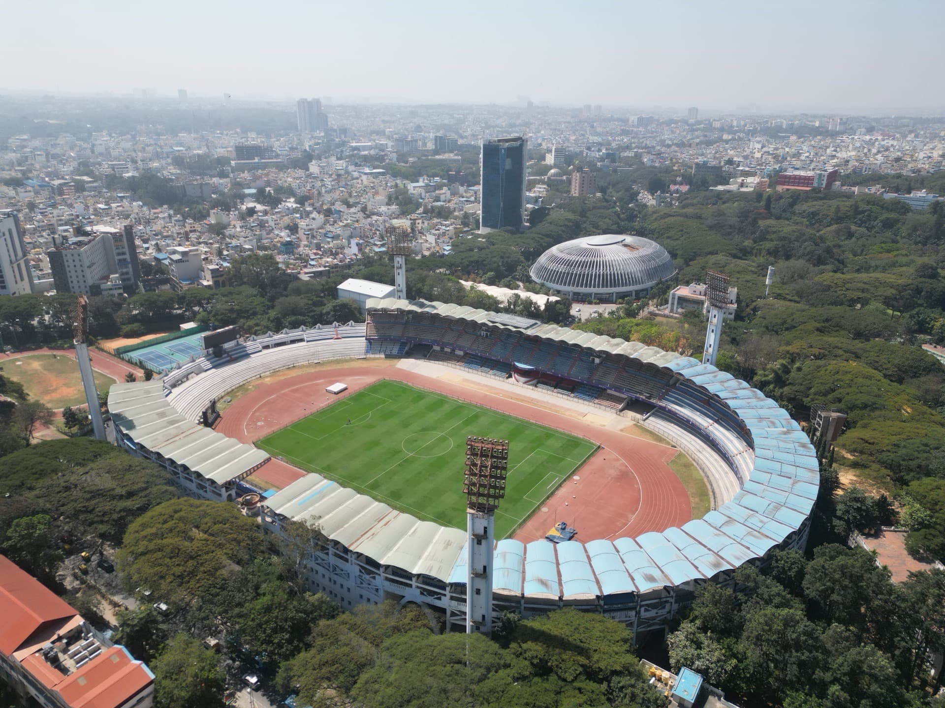 High-altitude aerial drone photo of a major stadium with running track, grass field, and surrounding city