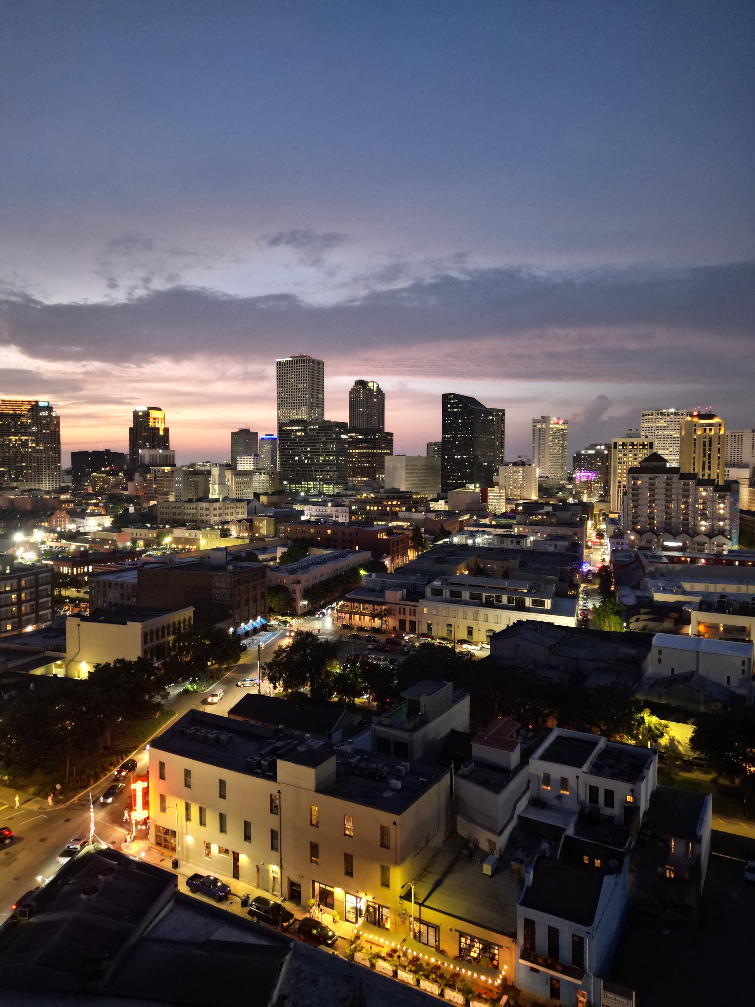 Aerial drone photo of New Orleans skyline at dusk with purple and pink sunset sky, city lights, and French Quarter streets