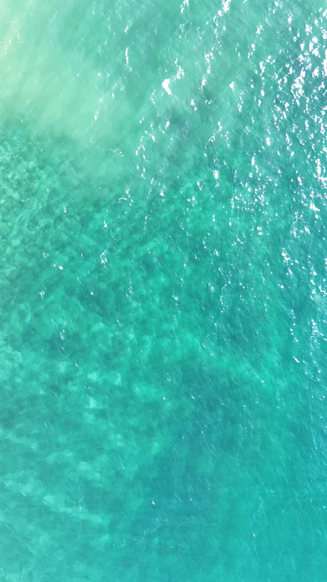 Straight-down overhead aerial of brilliant turquoise ocean water with light patterns and surface reflections