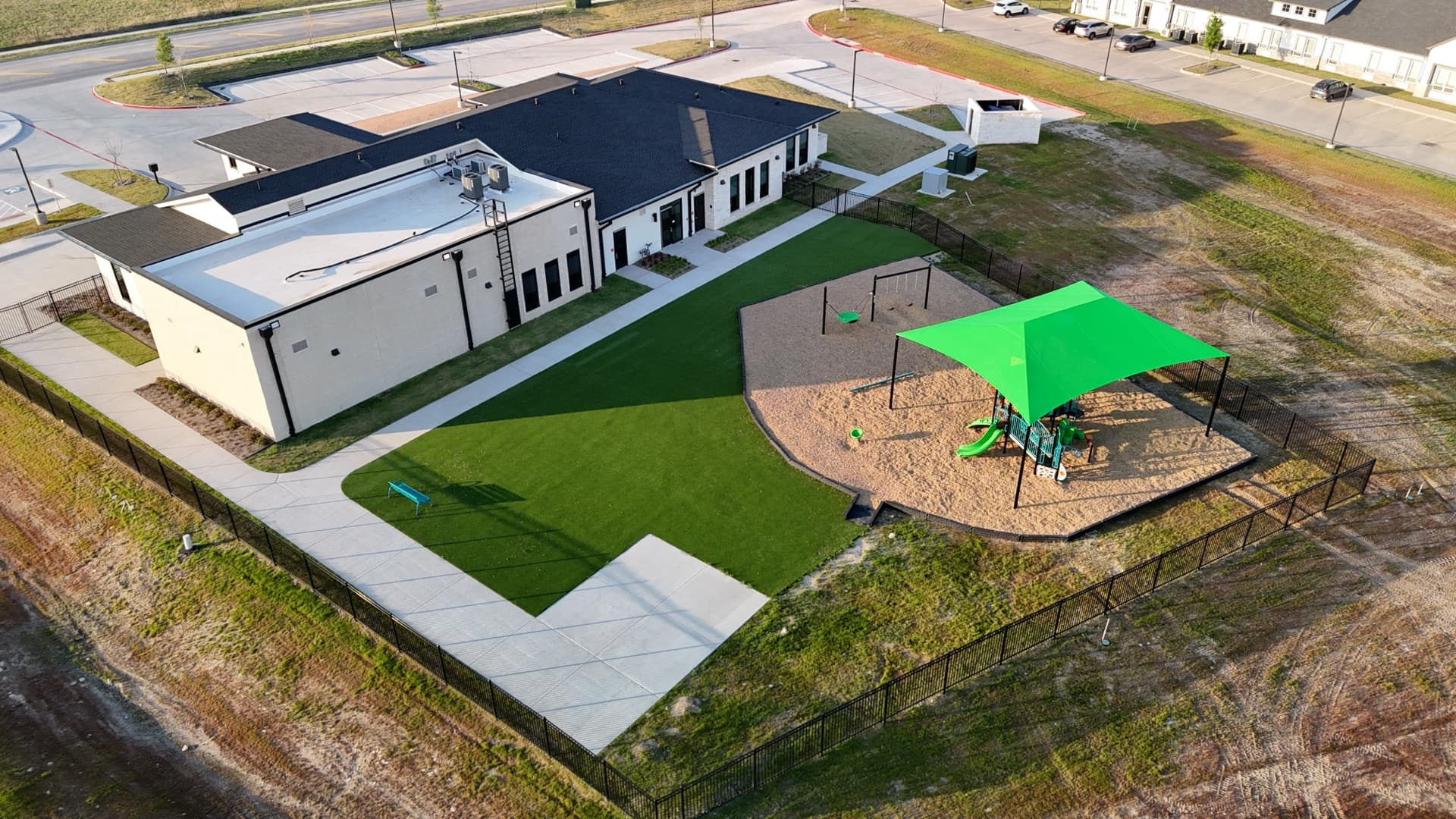 Aerial drone photo of school or daycare building with bright green shade structure over playground equipment and turf