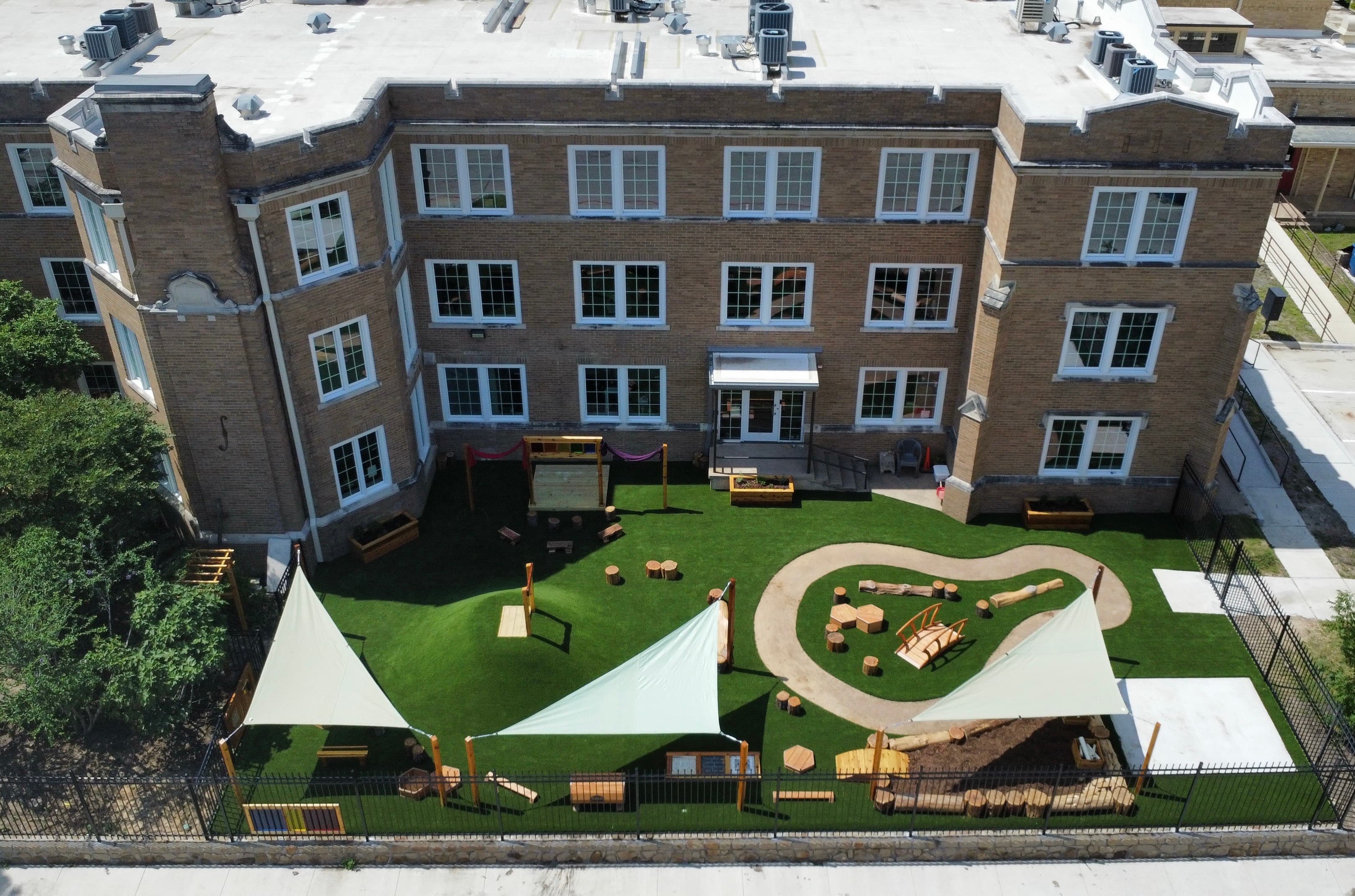 Aerial view of school campus showing new playground with artificial turf, sail shade structures, and natural play elements