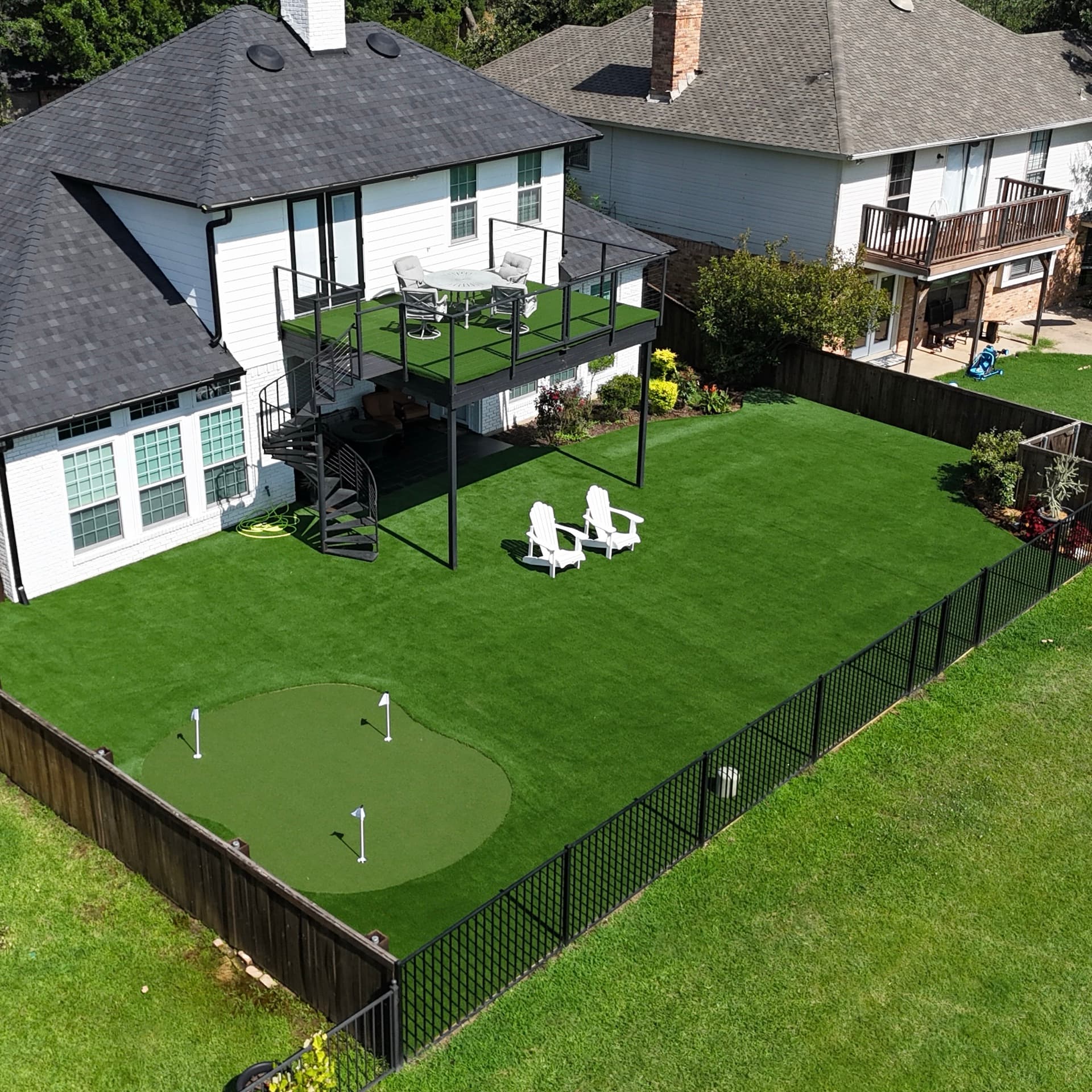 Aerial drone photo of suburban home backyard with artificial turf, putting green, elevated deck with outdoor furniture