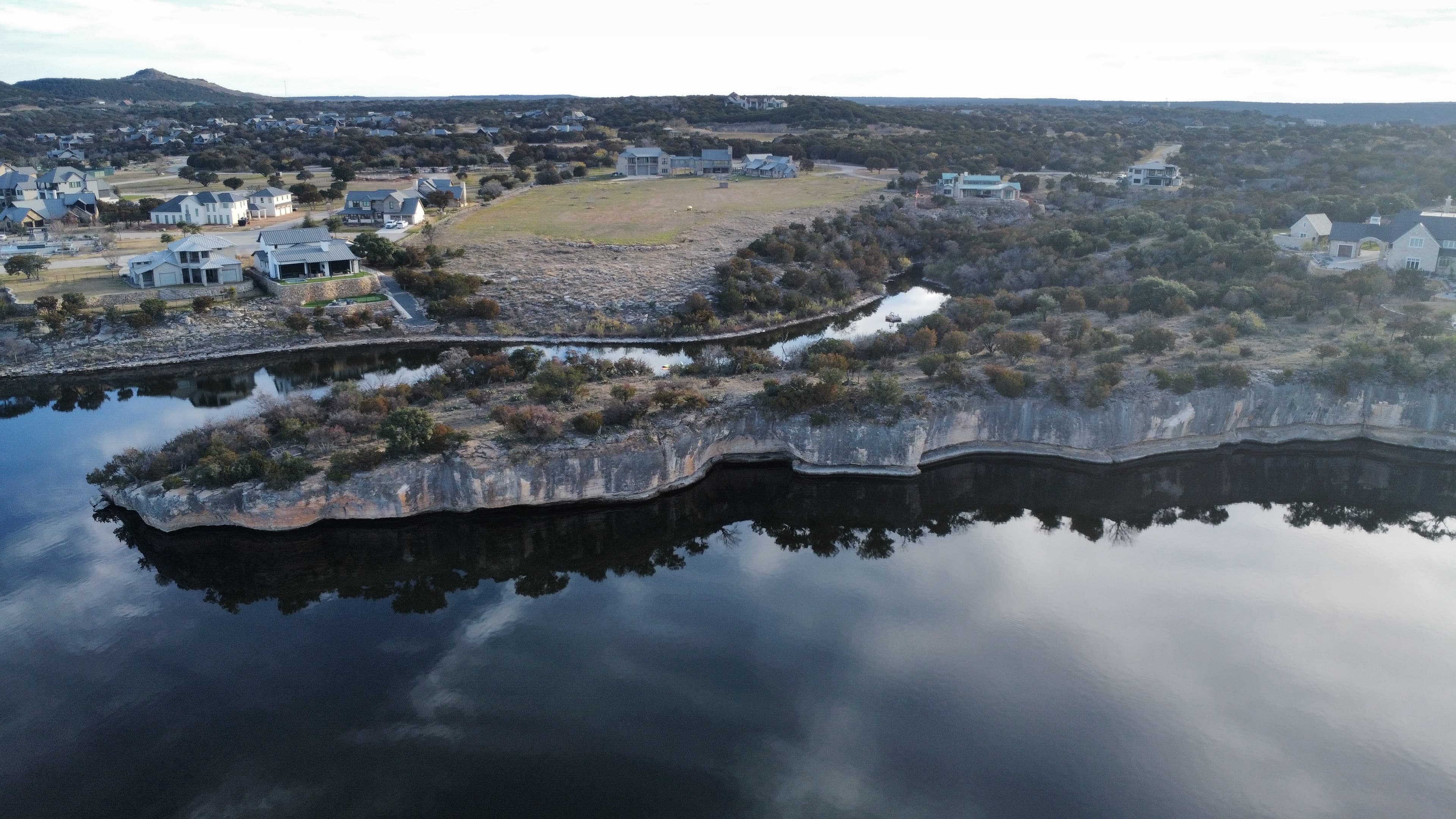 Aerial drone photo of Texas lake property with limestone bluffs, residential development, and glass-still water reflections