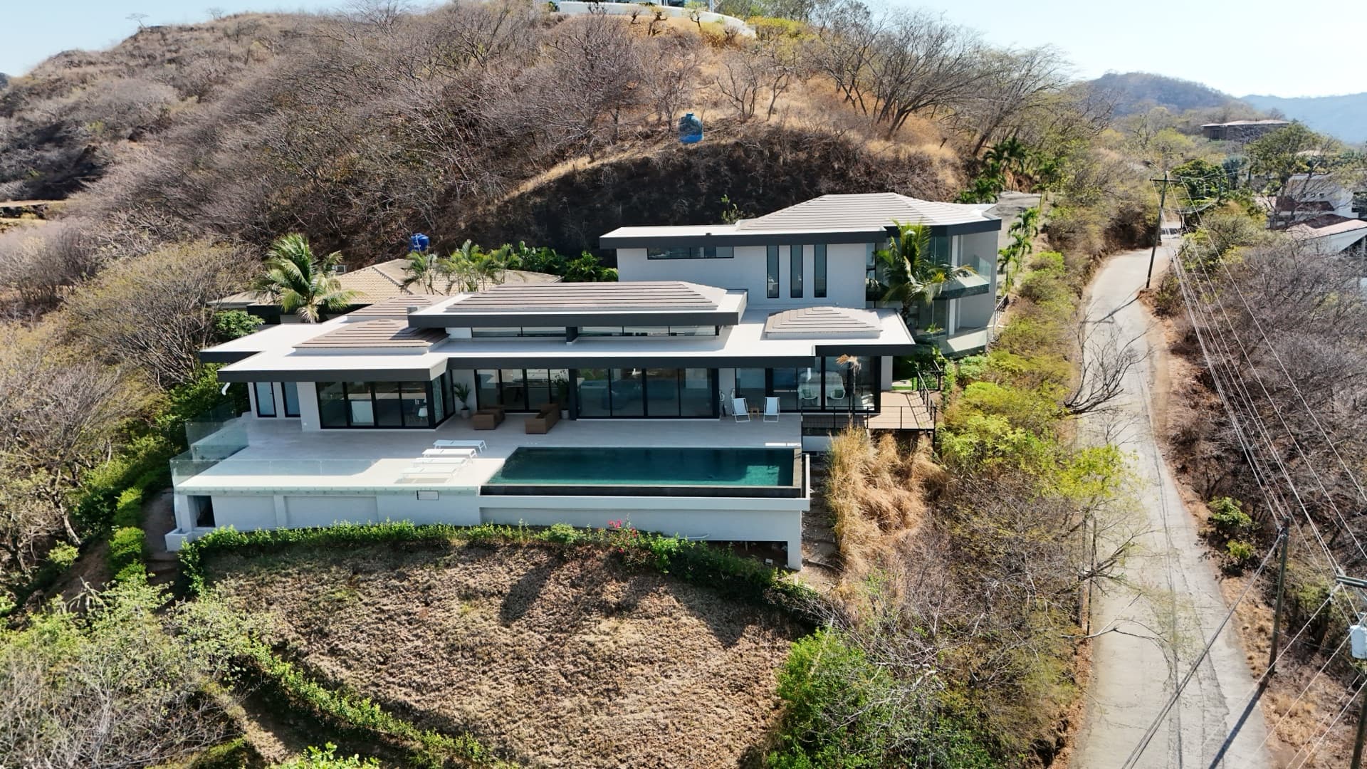 Aerial drone photo of modern luxury villa with infinity pool on a hillside overlooking a tropical coastline